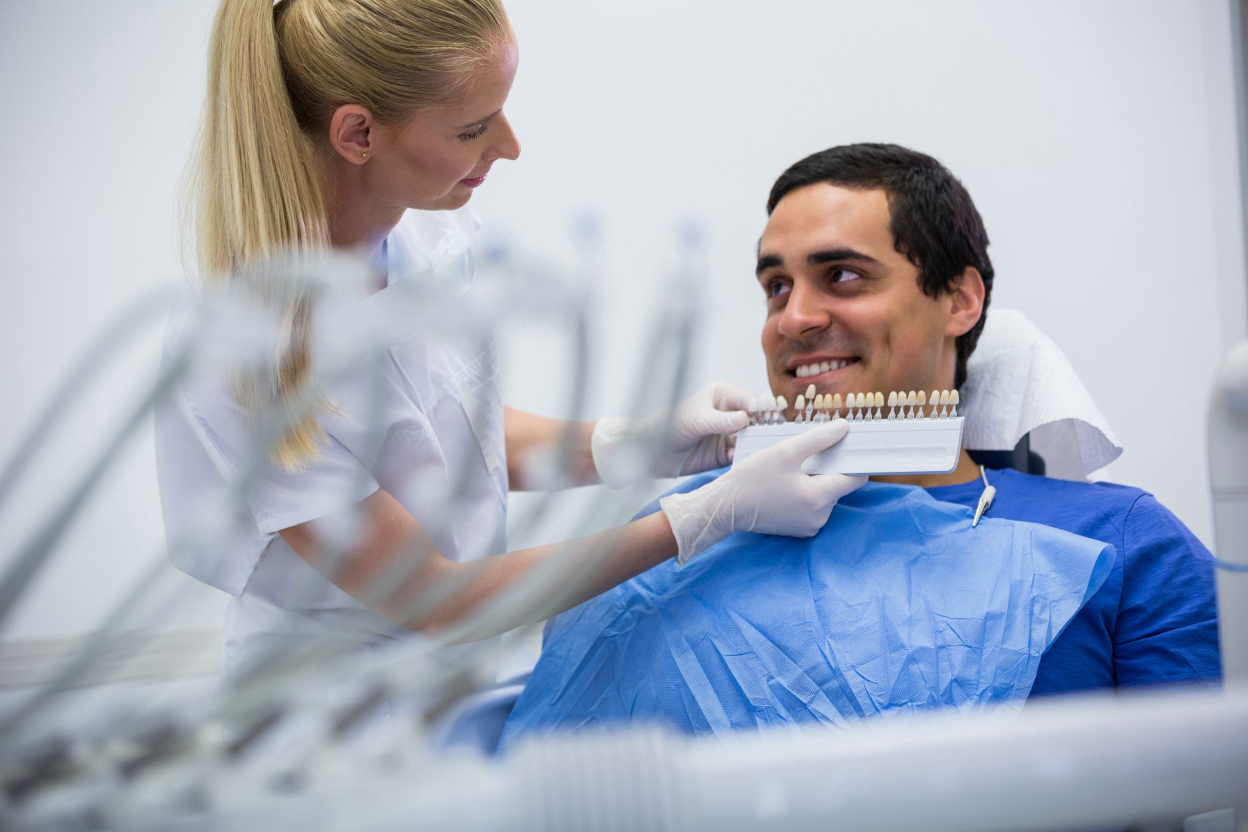 Dentist examining female patient with teeth shades at clinic