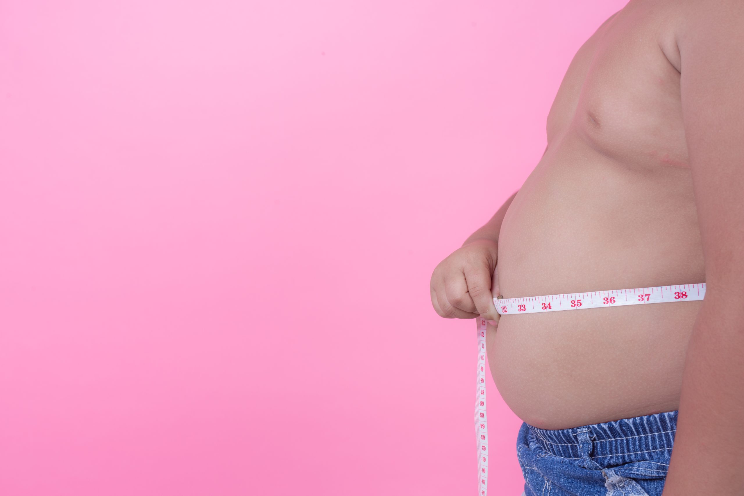 Obese boy who is overweight on a pink background.