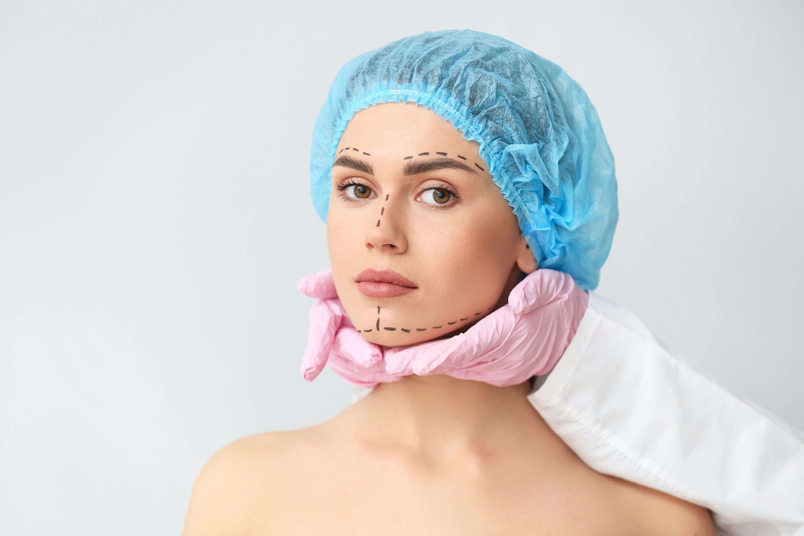 Plastic surgeon touching face of young woman on light background